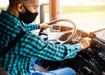 Man wearing a mask driving a semi truck
