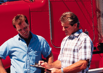 Two men looking at a clipboard in front of a red semi truck Two men looking at a clipboard in front of a red semi truck